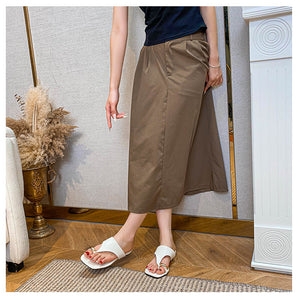 White toe-post flat sandals worn with a brown skirt