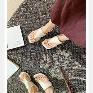 White gold buckle toe-post sandals worn on a patterned rug
