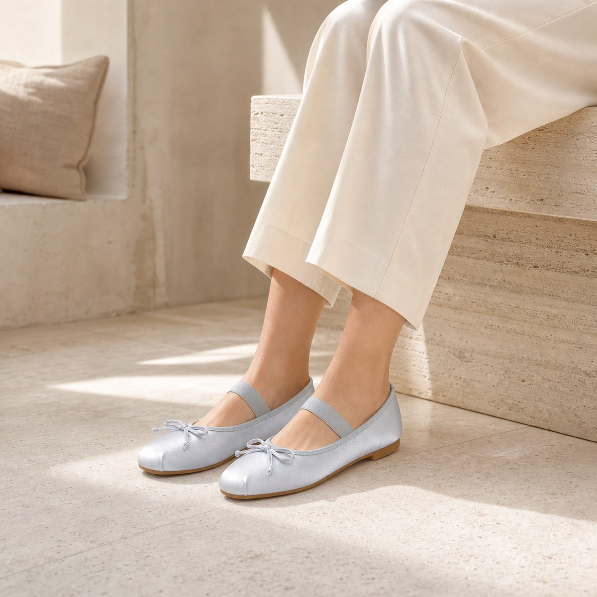 Woman wearing silver satin bow Mary Jane ballet flats in a warm travertine interior